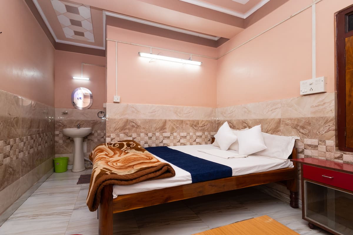 A bedroom with a bed, a bedside table, a mirror, a sink, and a green bucket.