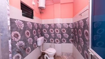 A bathroom with a pink and gray floral tile design, a white toilet, and a shower area.
