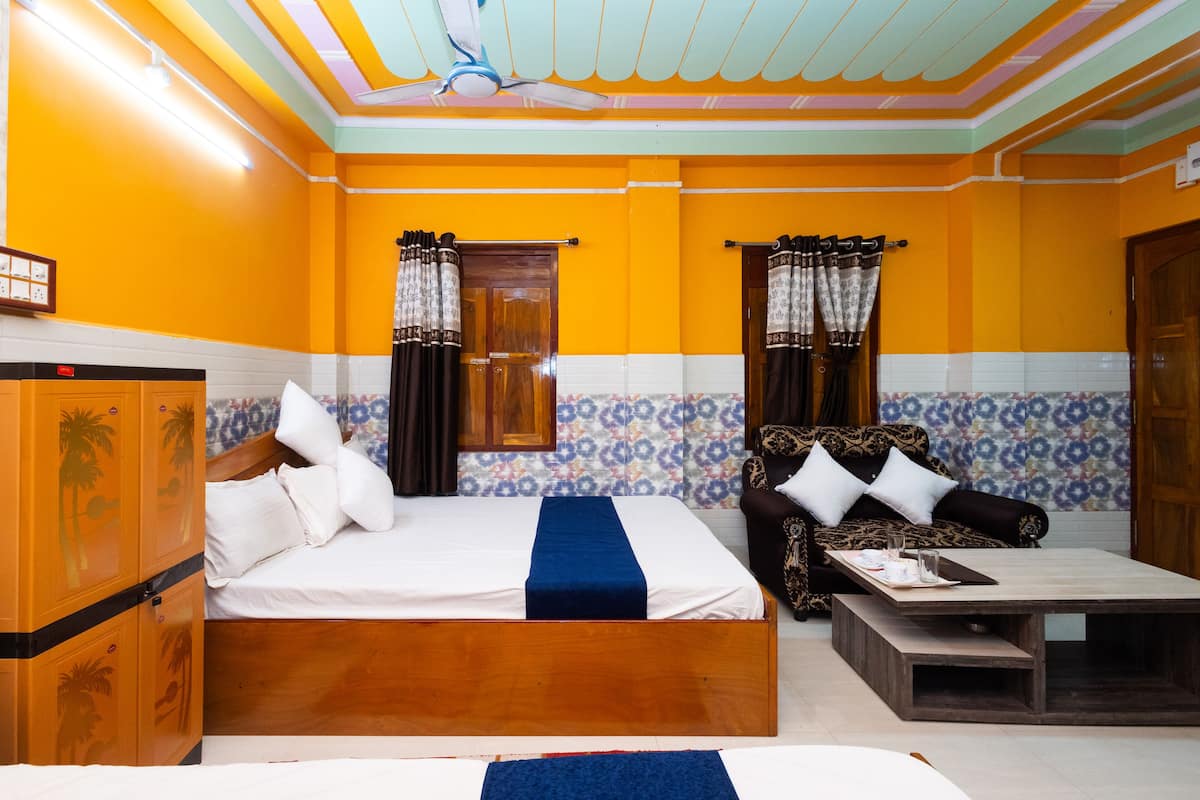 A hotel room with two beds, a wooden wardrobe, a sofa, a coffee table, and patterned curtains.