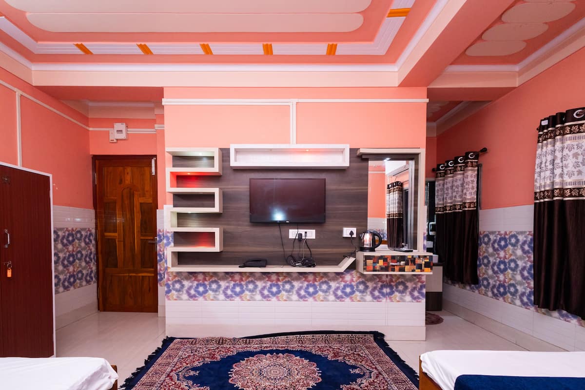 A hotel room with a TV mounted on the wall, a small desk with a telephone, and a patterned rug on the floor.