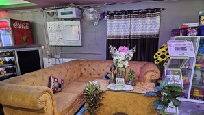 A living room with a brown sofa, a small table with decorative items, and a potted plant. - RAJA HOTEL AND LODGE  (Kharagpur)