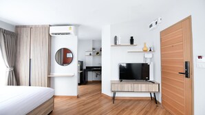 A modern hotel room with a bed, a TV, a desk, a mirror, and a kitchen area in the background. - You Hotel (Bangkok)