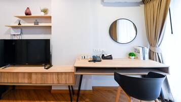 A modern room with a wooden desk, a black chair, a TV, a mirror, and a shelf with decorative items.