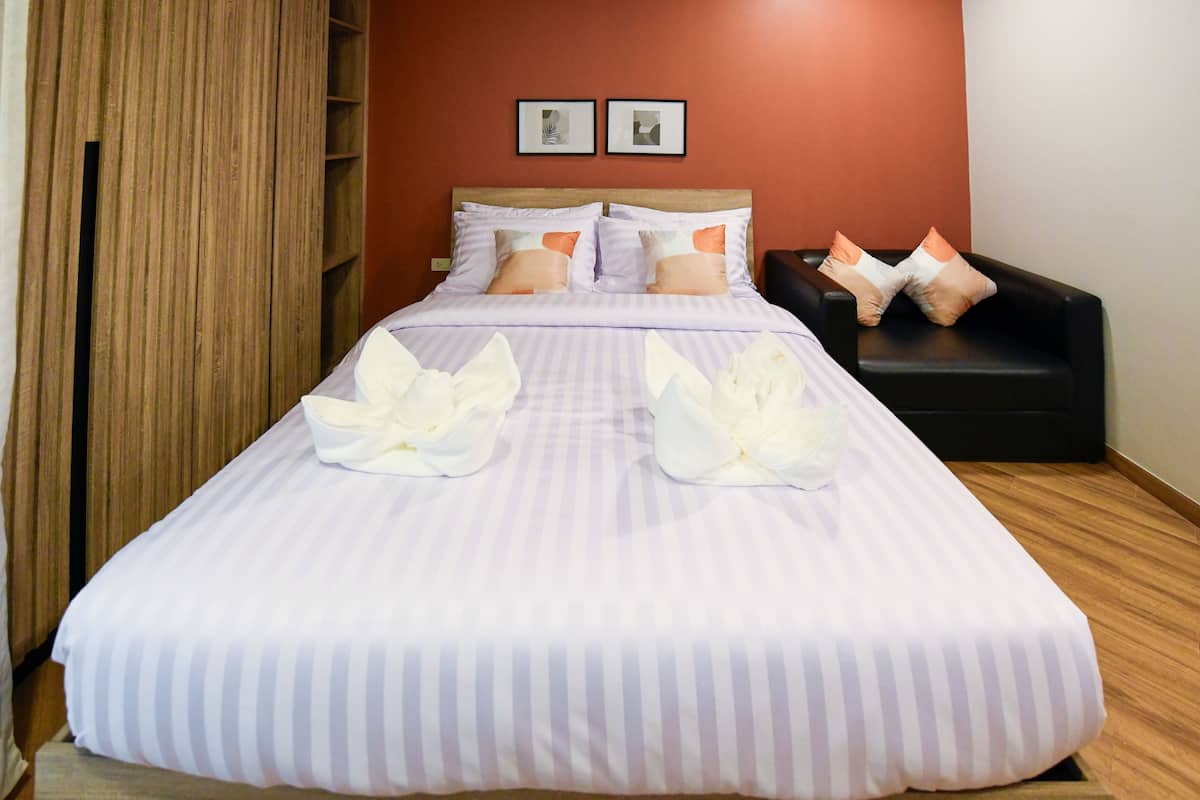 A neatly made bed with striped bedding and decorative pillows, a wooden headboard, and a black armchair with cushions.