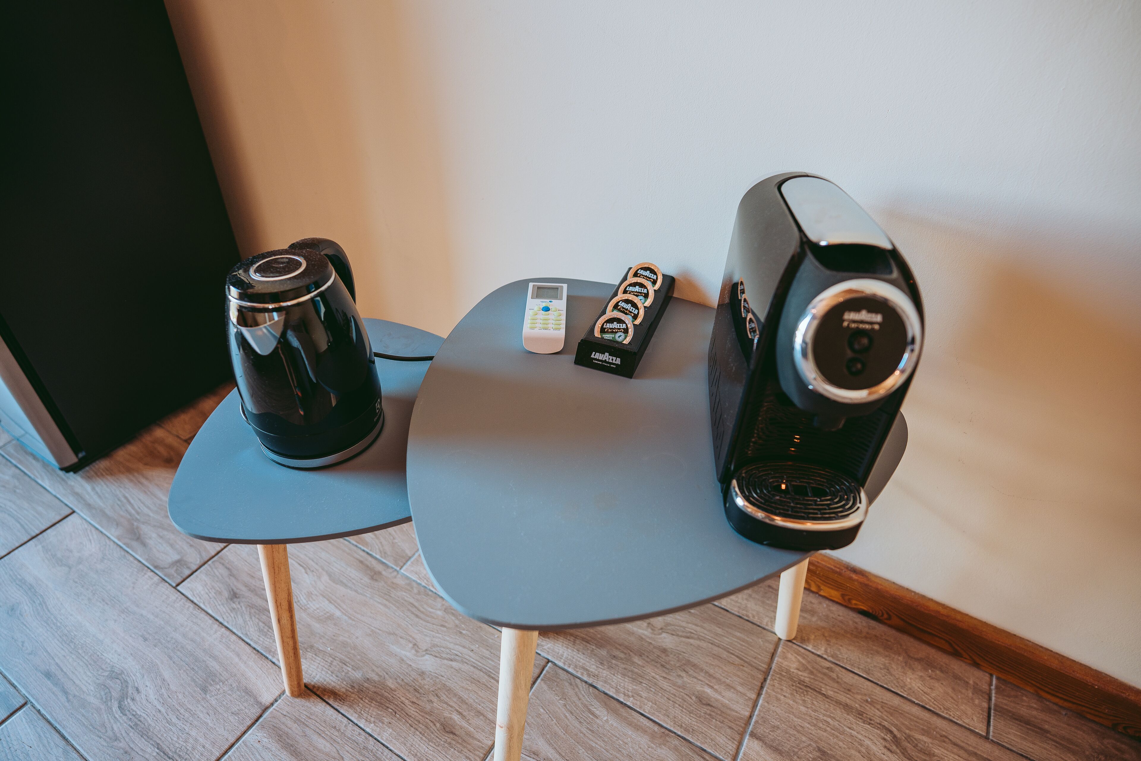 A coffee maker, a remote control, and a coffee pod dispenser on a small table.