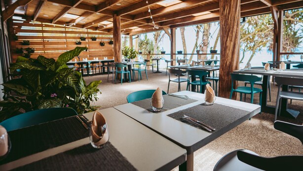 Un restaurante con vigas de madera en el techo, sillas verdes y mesas con manteles individuales y servilletas.