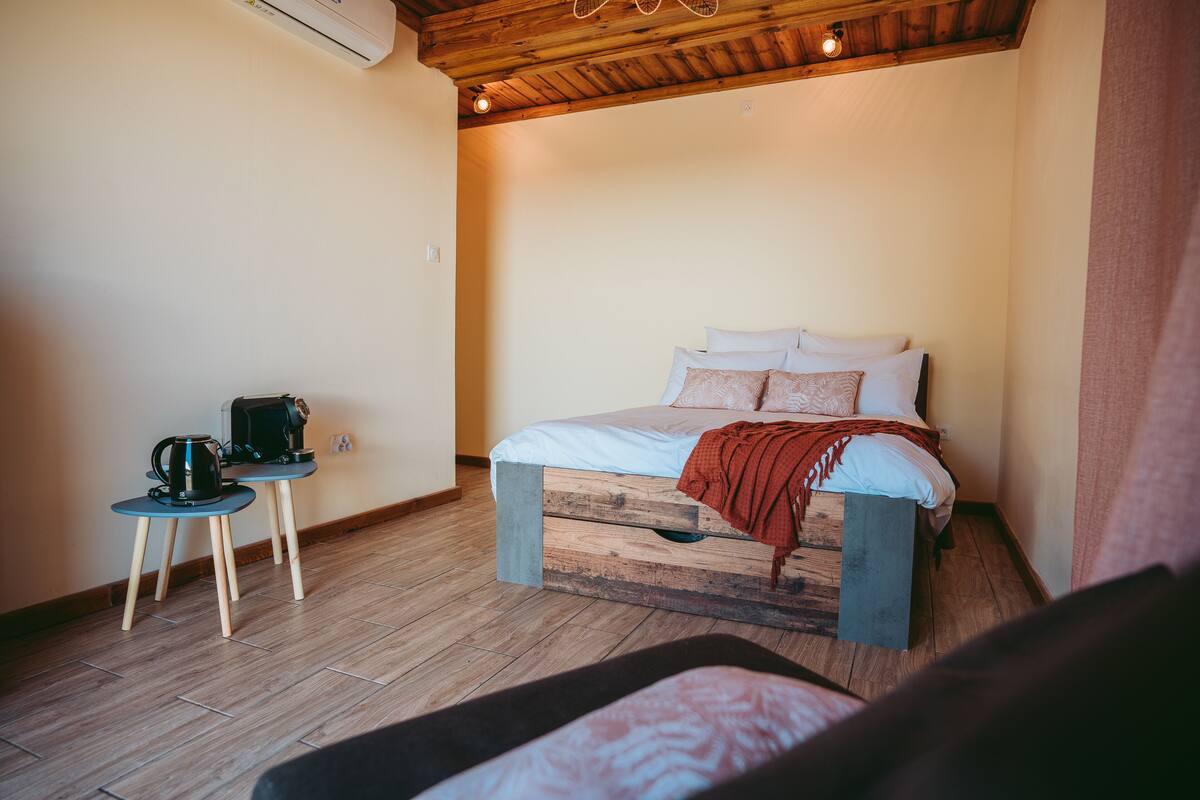 Une chambre avec un lit, une petite table sur laquelle se trouvent une bouilloire et une machine à café, et un plancher en bois.