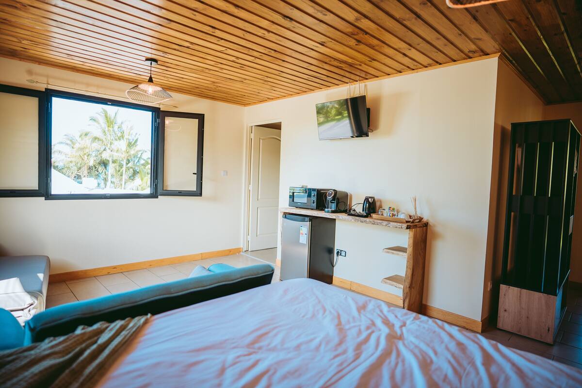 Une chambre avec un lit, un bureau doté d’un micro-ondes, une télévision et une fenêtre donnant sur des palmiers.