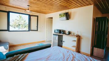 A room with a bed, a desk with a microwave, a television, and a window with a view of palm trees.