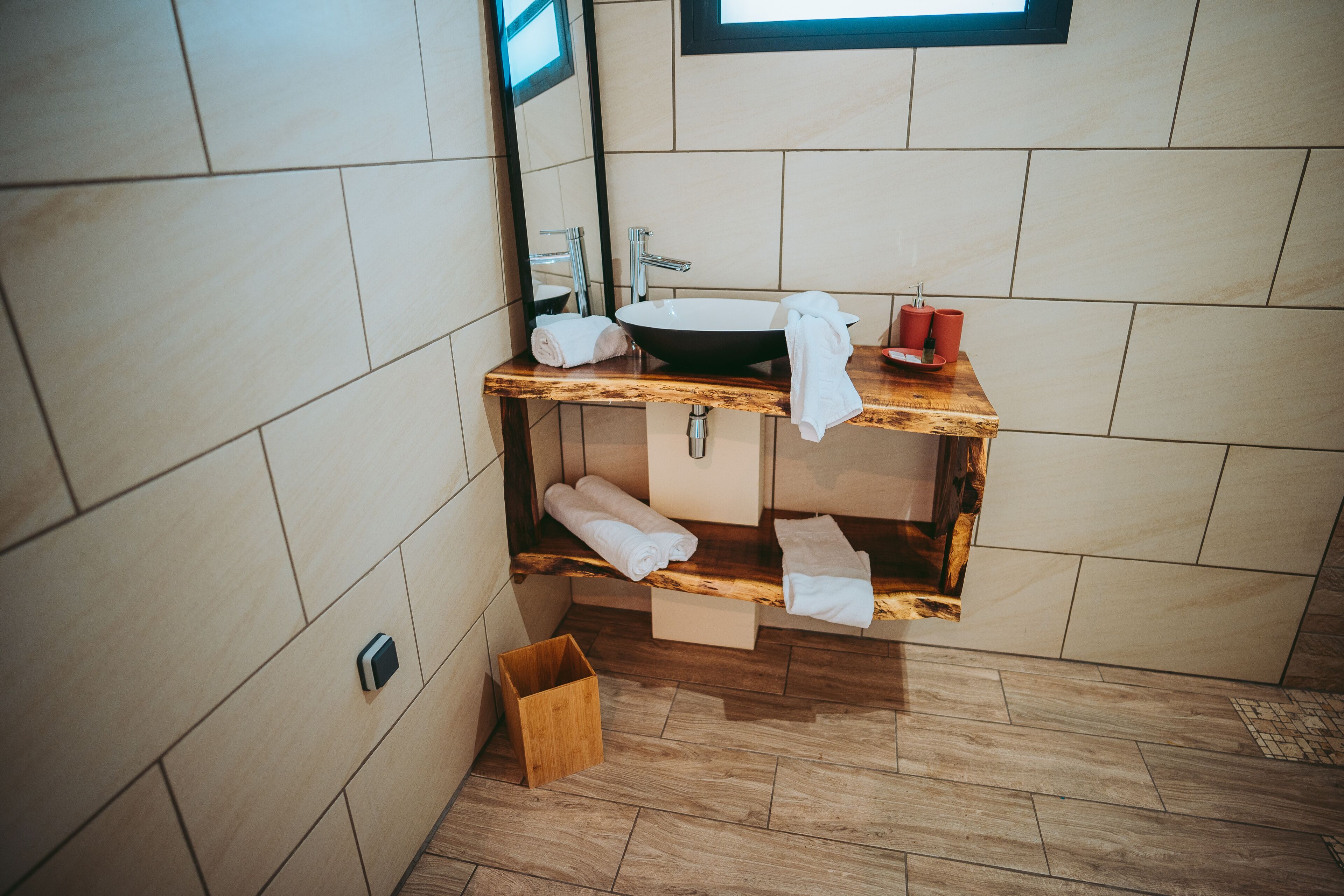 Une salle de bain moderne avec un meuble-lavabo en bois, un grand miroir, un évier et des serviettes soigneusement pliées.