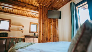 Un dormitorio con techo de madera, una cama, un televisor montado en la pared y un ventanal con cortinas.