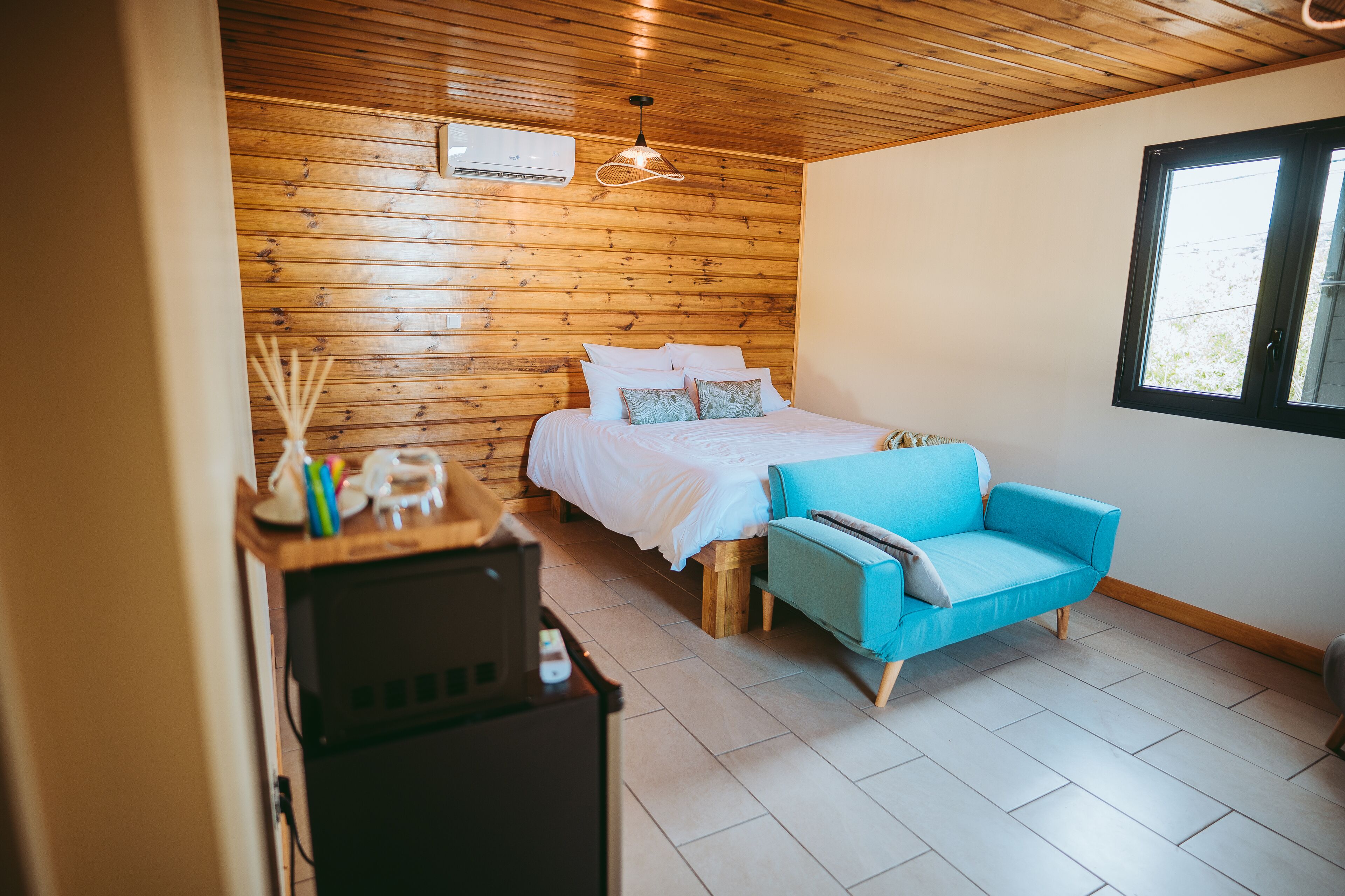 Une pièce avec un plafond en bois, un lit avec une literie blanche, un canapé bleu et une fenêtre.
