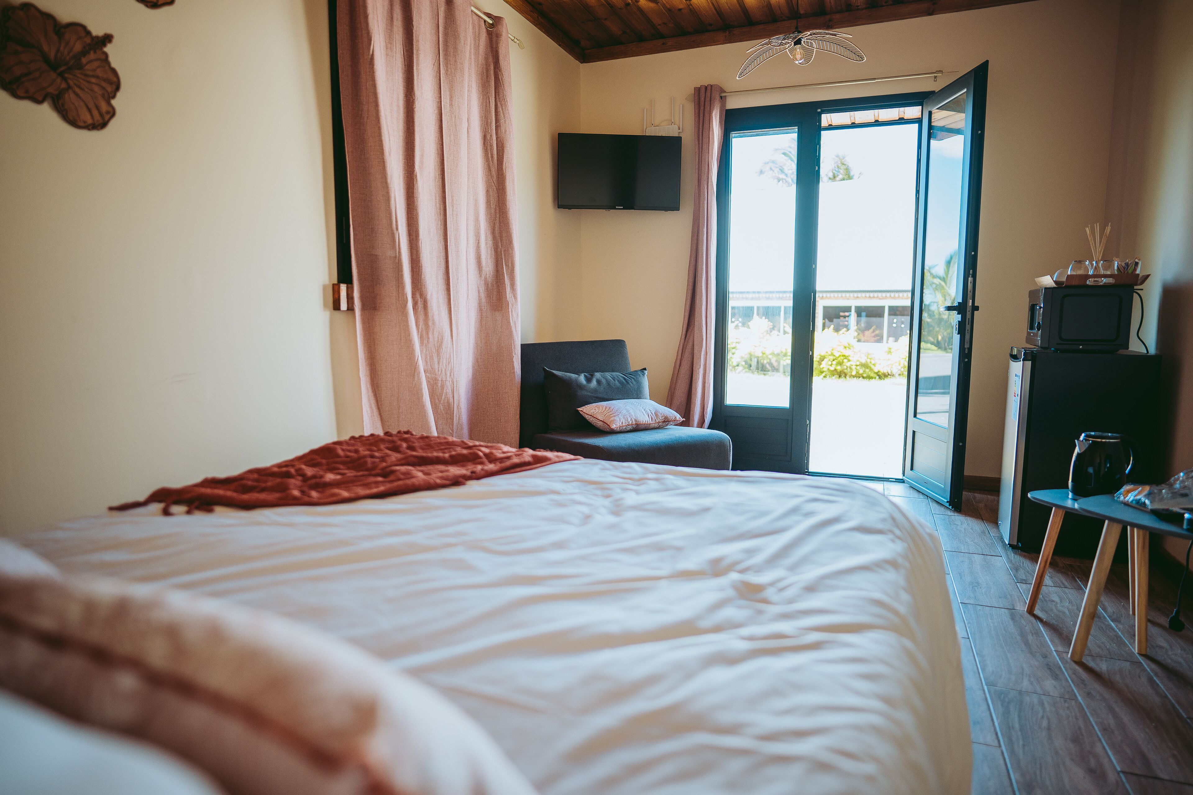 A bedroom with a bed, a chair, a TV, and a balcony with a view.