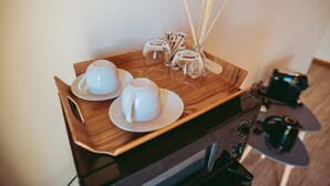 Una bandeja de madera con dos tazas y platillos blancos, un recipiente de vidrio con palitos de juncos y un objeto negro pequeño sobre una mesa.