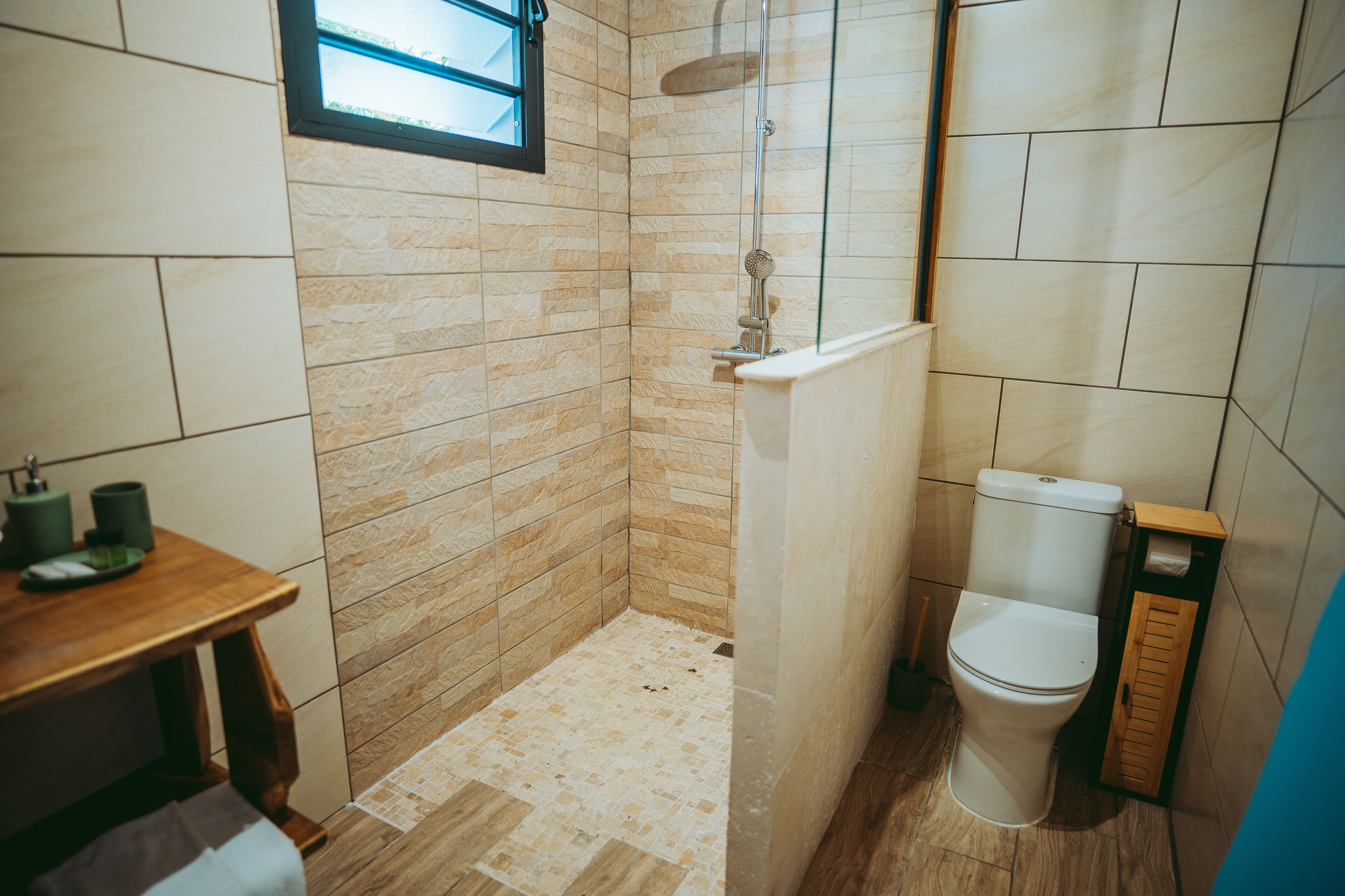 A bathroom with a shower, toilet, and a small table with a towel.