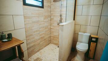 A bathroom with a shower, toilet, and a small table with a towel.