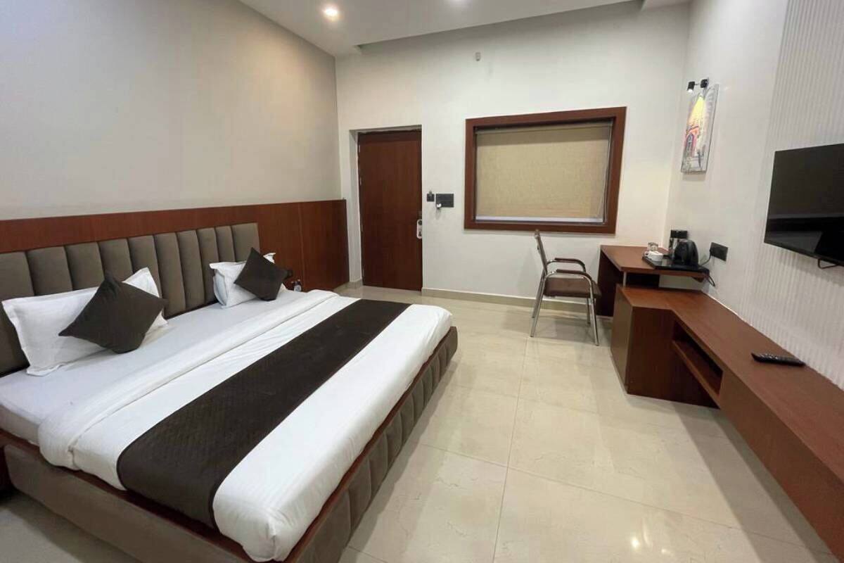 Une chambre d’hôtel avec un grand lit, un bureau, une chaise, une télévision et une fenêtre avec des stores.