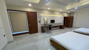 A modern hotel room with a large bed, a desk with a chair, a television, and a wardrobe. - The Kedar Resort (Mathura)
