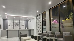 A modern hotel reception area with a marble reception desk, seating area, and large windows. - Genio Syariah Hotel Solo (Surakarta)