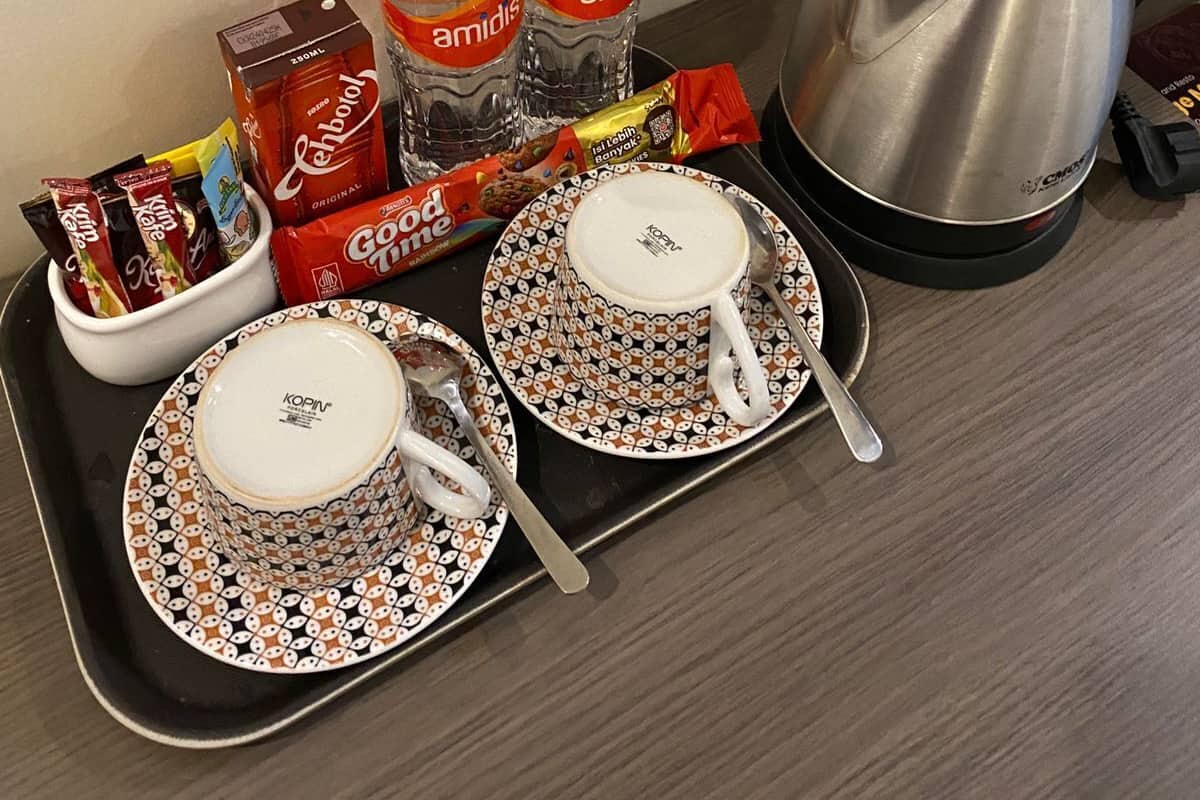 Una bandeja con cafetera, dos botellas de agua, una caja de café instantáneo, una bolsita de té y dos tazas con platillos.