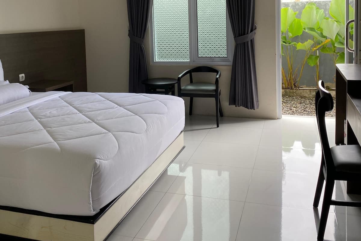 Una habitación de hotel con una cama grande, un escritorio, dos sillas y un ventanal con cortinas.