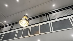 A chandelier hanging from the ceiling in a room with a high ceiling and a balcony with a mesh railing. - Genio Syariah Hotel Solo (Surakarta)