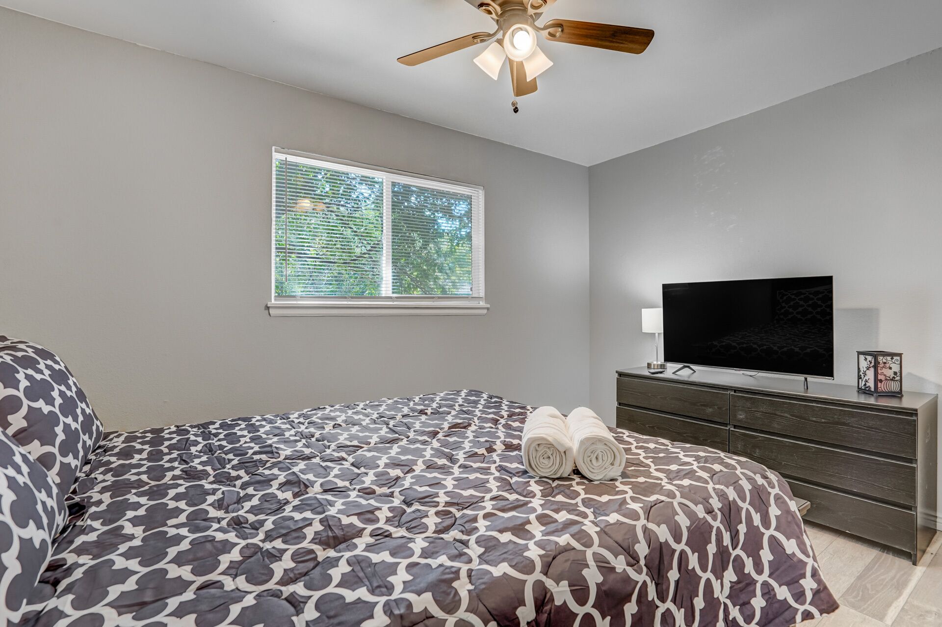 A bedroom with a bed, a TV, a dresser, and a ceiling fan.
