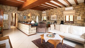 A spacious living area with a stone wall, wooden ceiling beams, a white sofa, a wooden coffee table, and a stone fireplace. - Beautiful, Unique, 'stone-built villa on the outskirts of Peyia  (Peyia)