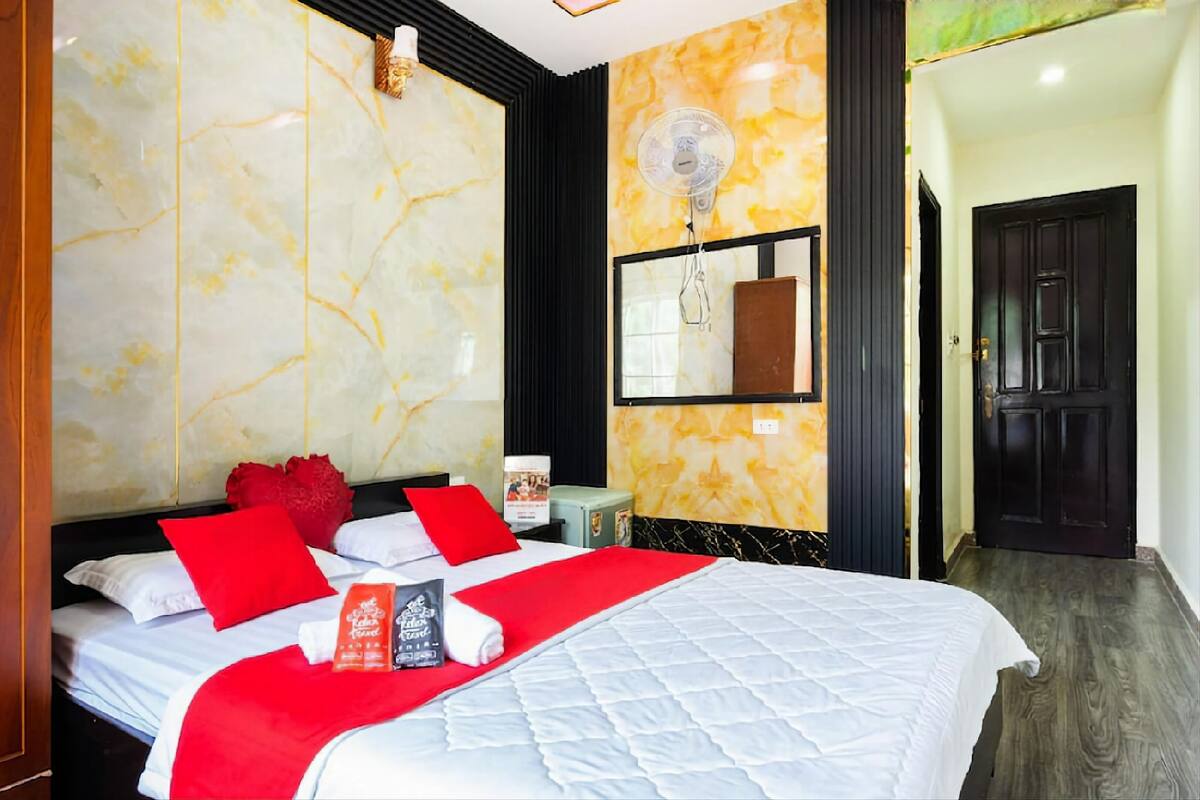 Habitación de hotel con pared de mármol, cama con ropa de cama roja y blanca, espejo con marco negro y puerta de madera.