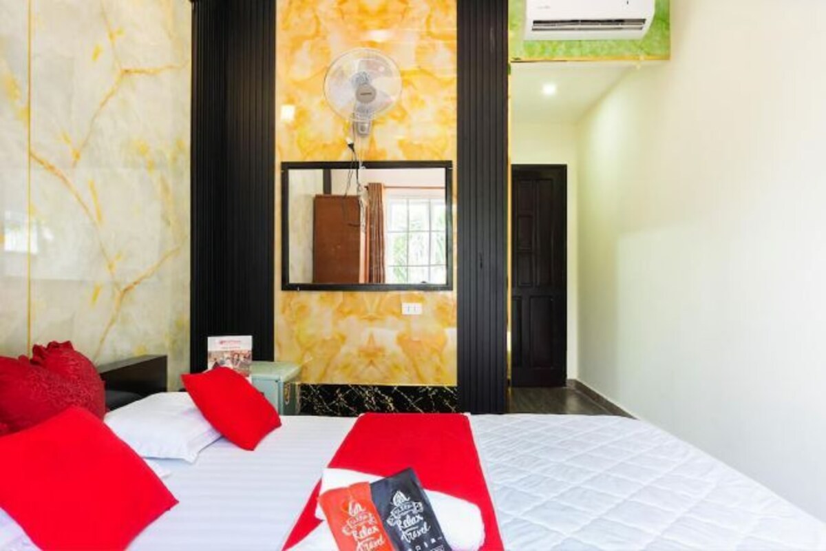 Een hotelkamer met een bed, rode kussens, een ventilator, een spiegel en een deur.