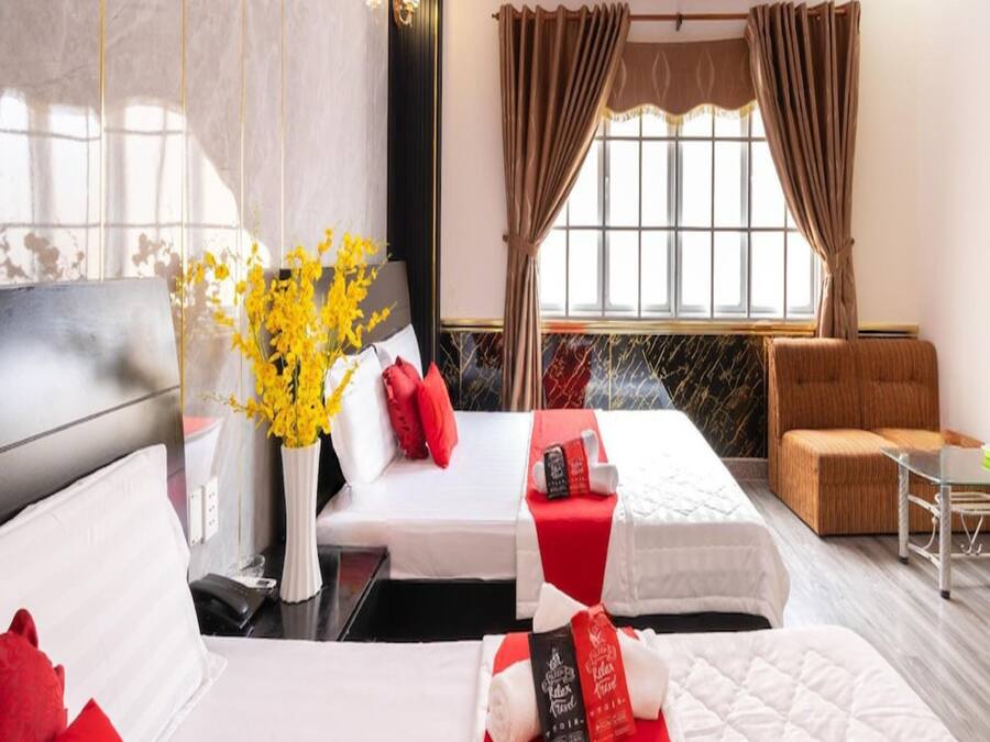 Una habitación de hotel con dos camas, un sofá, una mesita y una ventana con cortinas.