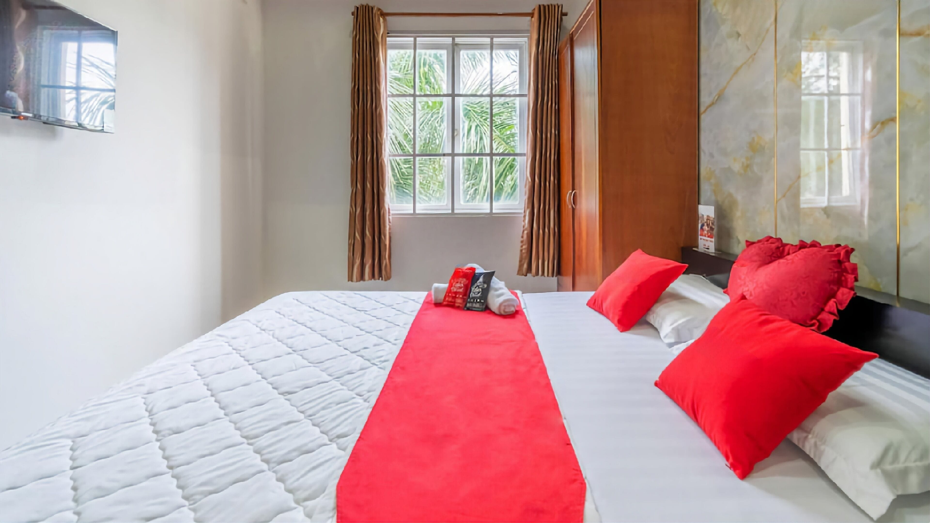 Een hotelkamer met een groot bed, rode kussens, een rood tapijt en een raam met gordijnen.