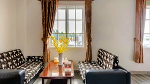 Una habitación con dos sofás estampados, una mesa de madera con un jarrón de flores amarillas y una ventana con cortinas.