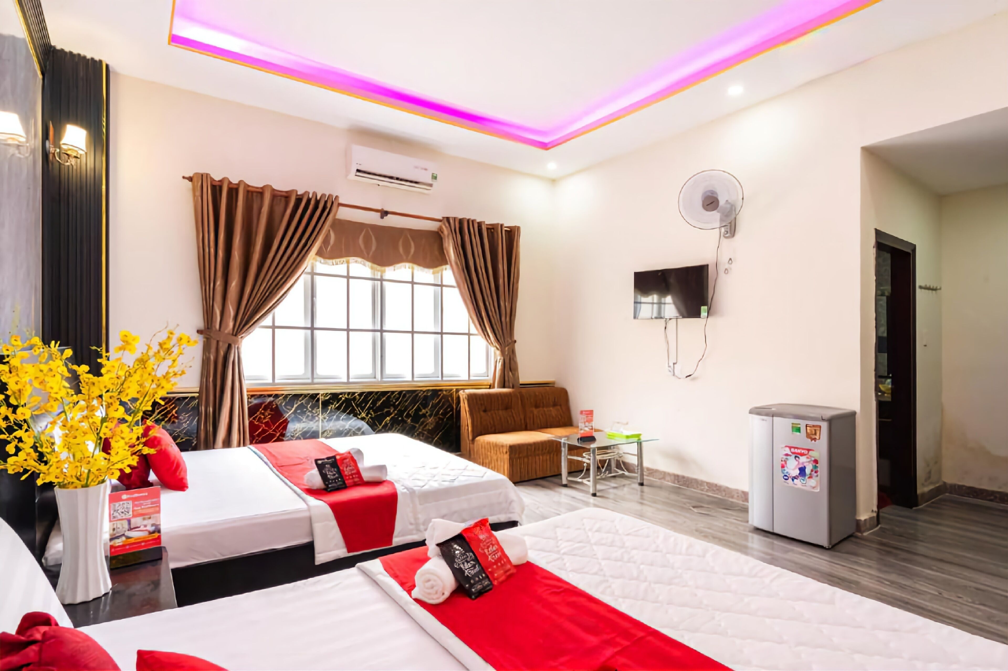 A hotel room with two beds, a sofa, a small table, a fan, and a refrigerator.