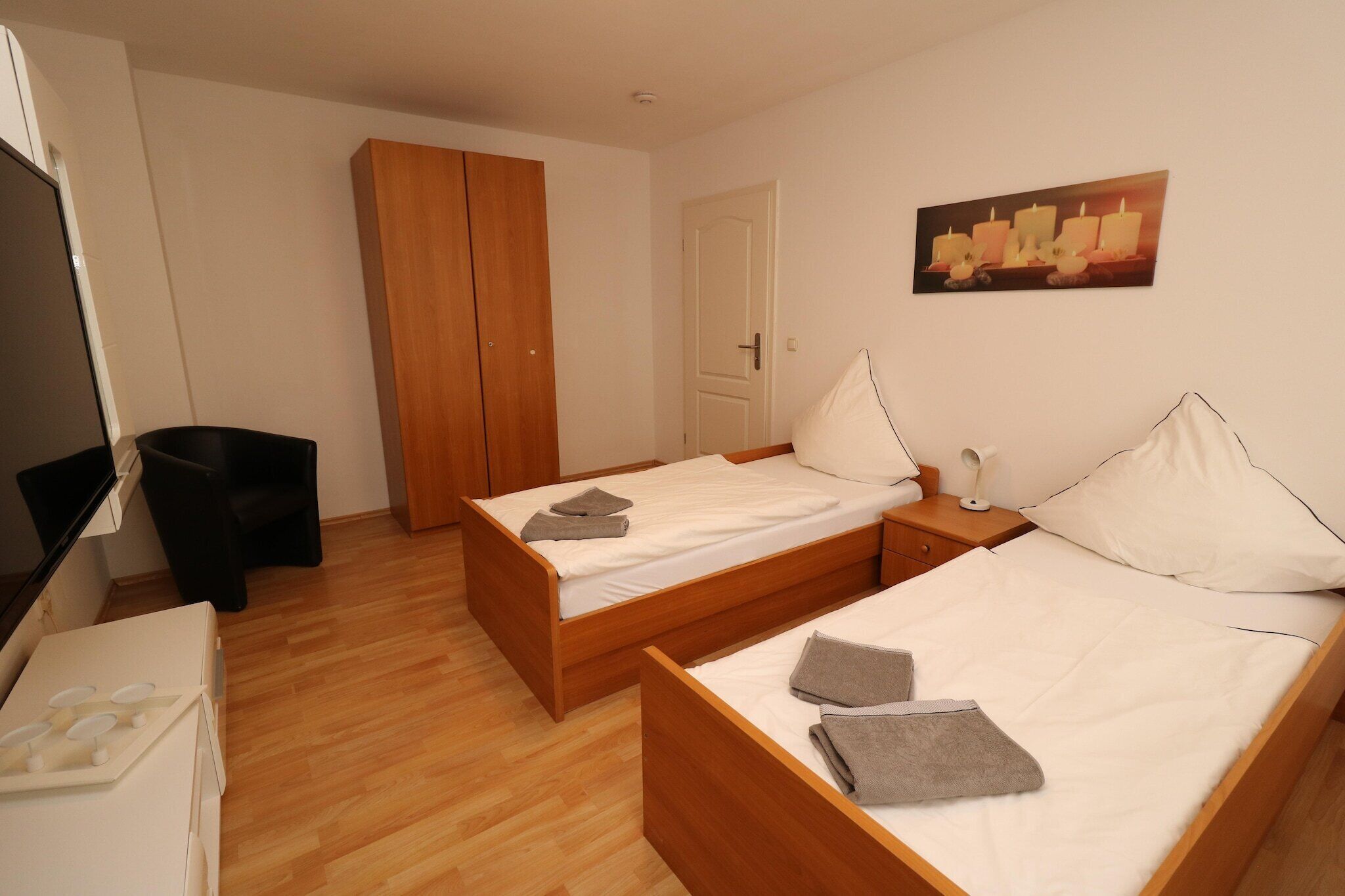 A bedroom with two beds, a wardrobe, a desk, and a television.