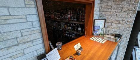 Una zona de bar con mostrador de madera, estantes llenos de botellas y un calendario en la pared.