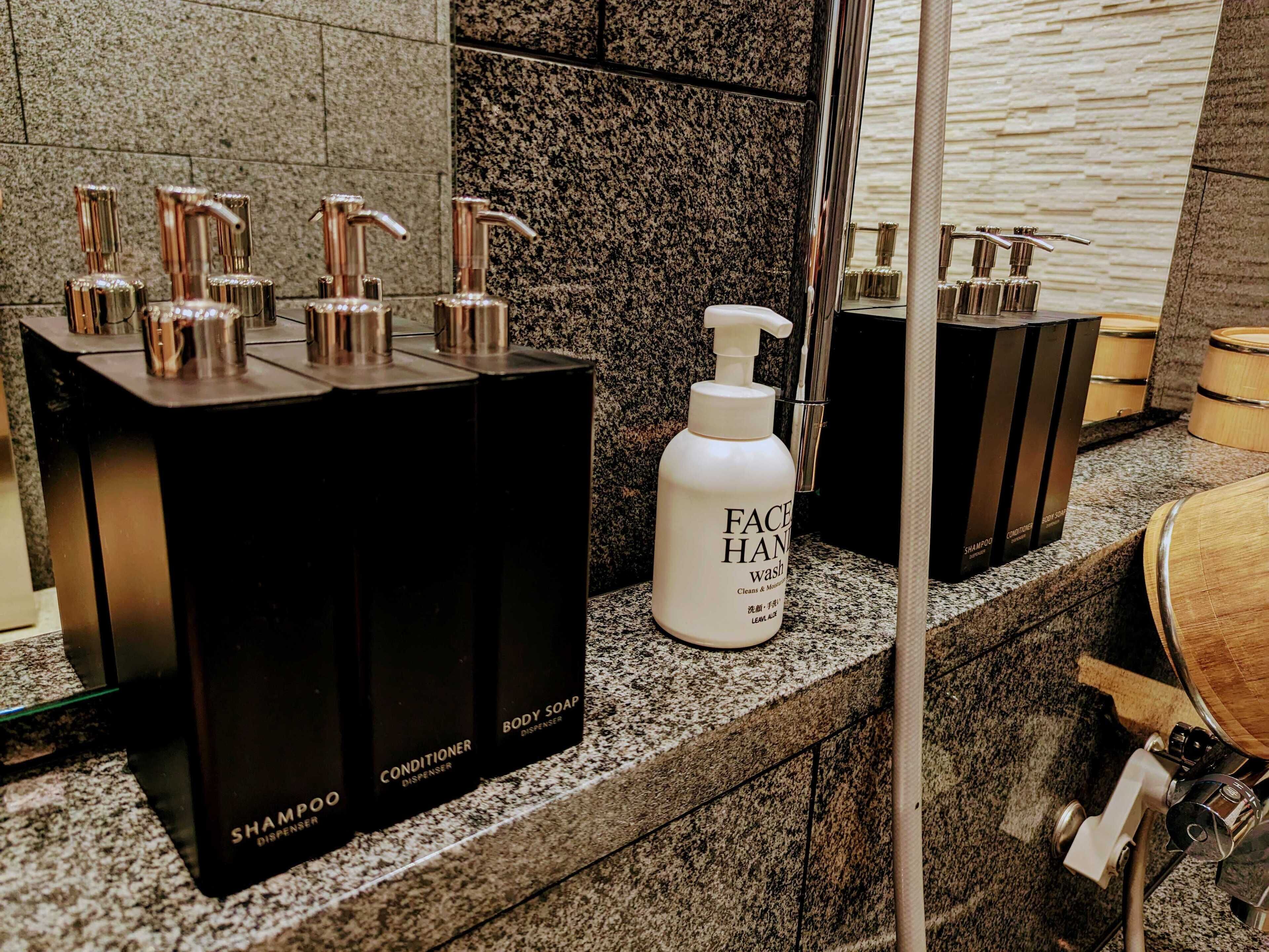 A bathroom with multiple dispensers for shampoo, conditioner, body soap, and face wash.