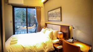 A hotel room with a large bed, a desk with a lamp, a chair, and a window with a view of trees. - Hotel Kaze no yama (Iida)