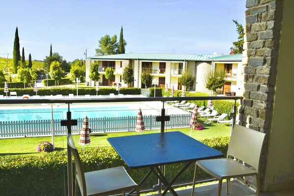 Relax on the balcony with a view of the pool surrounded by lounge chairs and umbrellas.