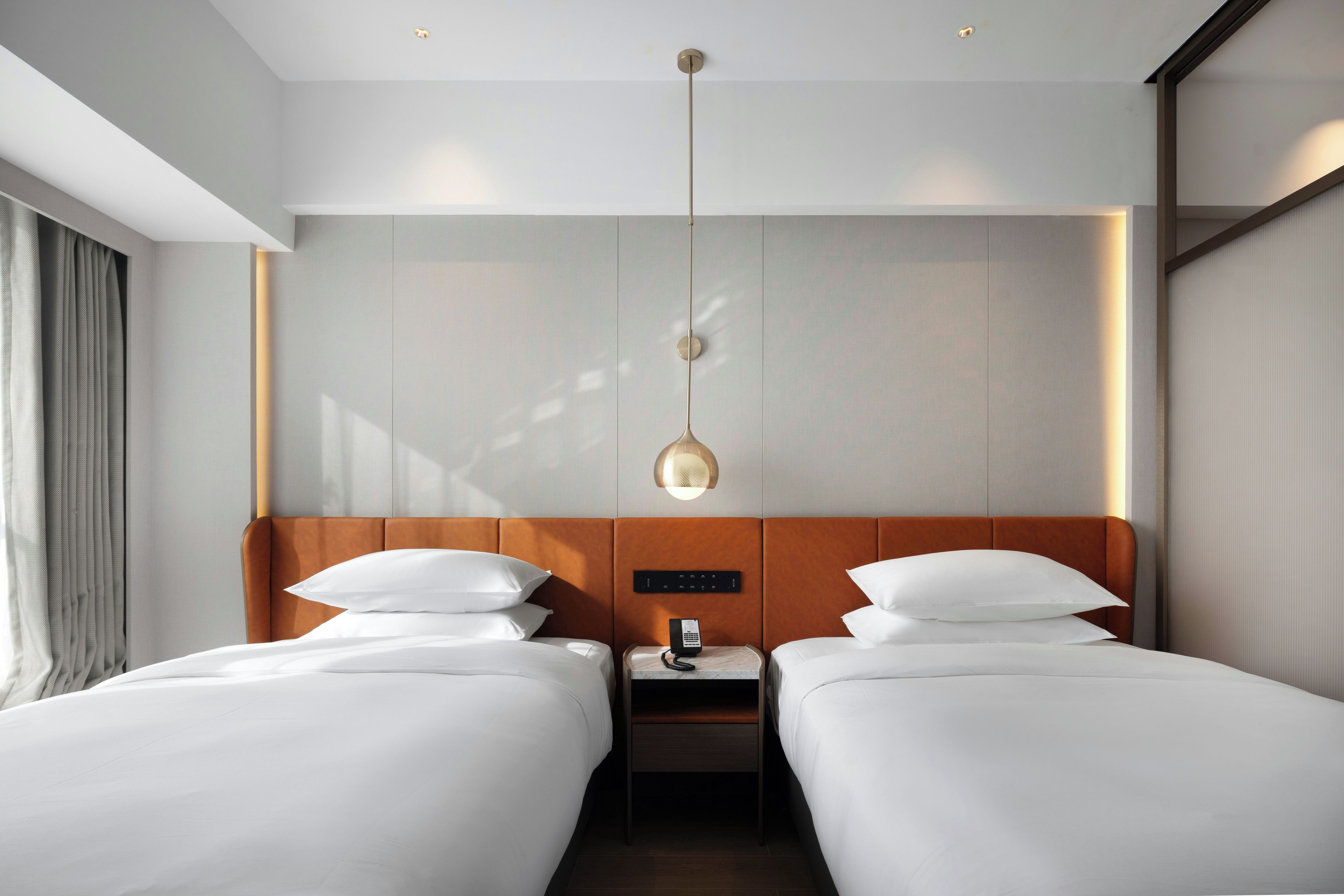 Habitación de hotel con dos camas, una mesita de noche, un teléfono y una lámpara fijada a la pared.