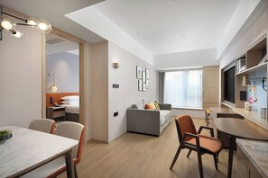 A modern hotel room with a dining area, a sofa, a bed, and a kitchen area.