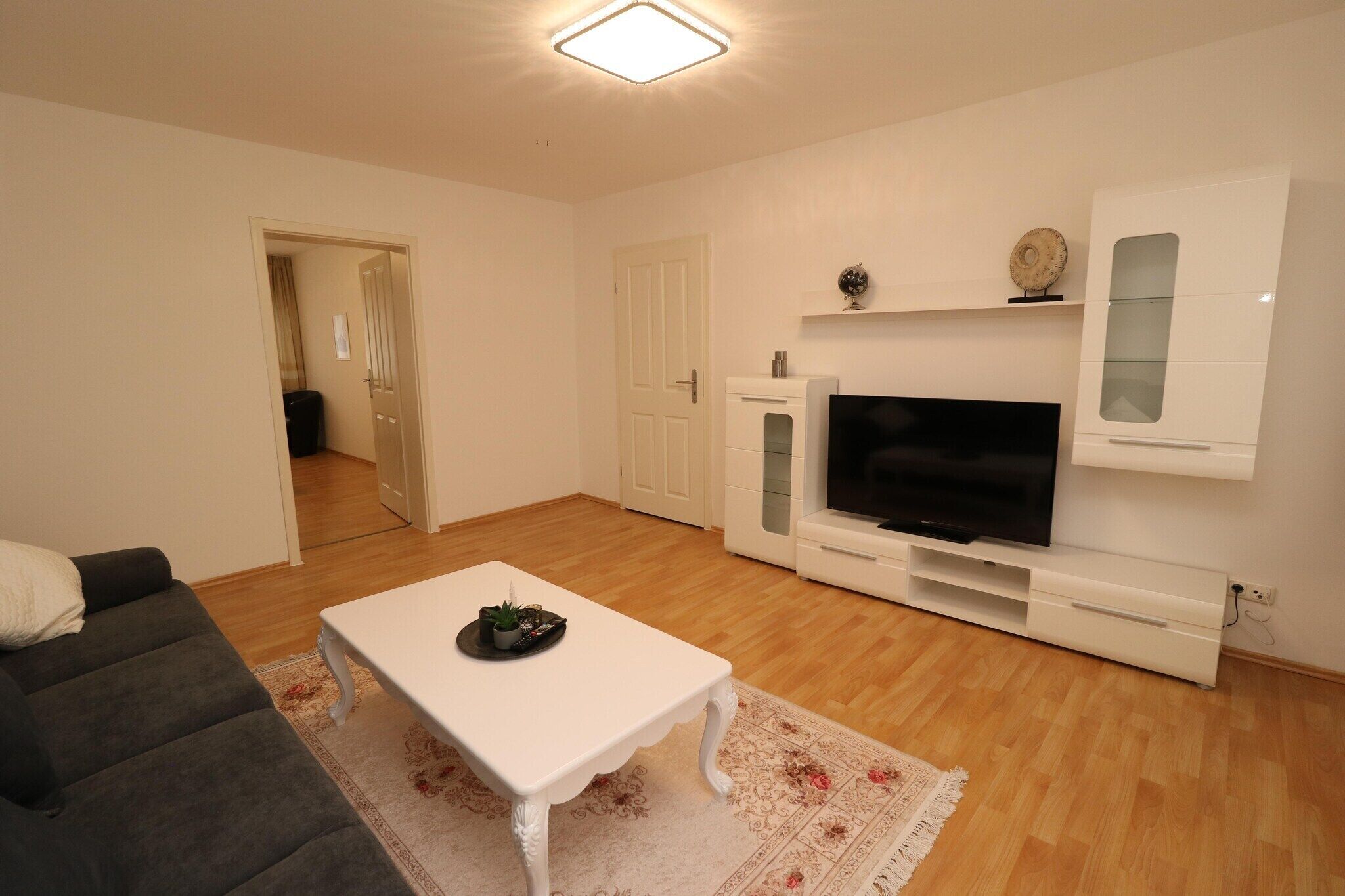 Un salon avec un canapé blanc, une table basse blanche, un téléviseur à écran plat et un meuble blanc avec des portes en verre.