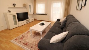 A living room with a grey sofa, a white coffee table, a flat-screen TV, a white cabinet, and a radiator. - Apartment in Essen with Balcony (Essen)