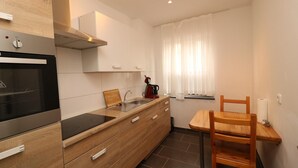 A modern kitchen with a built-in oven, wooden cabinetry, a sink, and a dining area with a chair. - Apartment in Essen near Messe Essen (Essen)