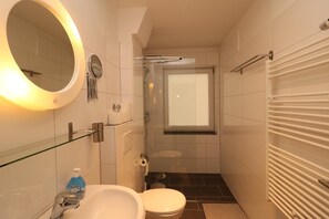 Un baño pequeño con cabina de ducha de vidrio, inodoro, lavamanos con espejo y toallero.