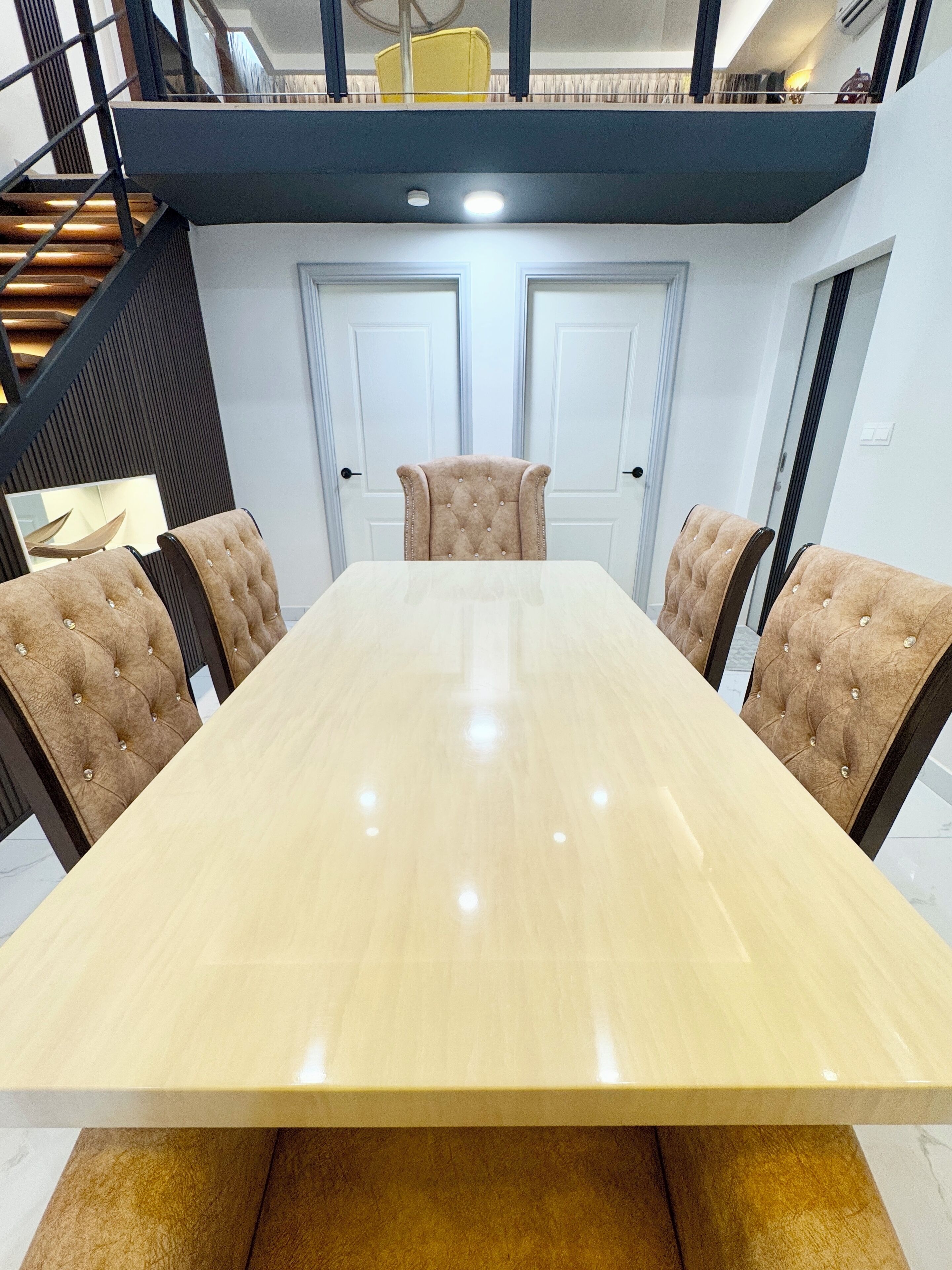 A conference room with a long table, six tufted chairs, and a staircase leading to an upper level.