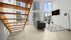 Un salon moderne avec un escalier, un canapé gris, une table basse et un téléviseur fixé au mur.