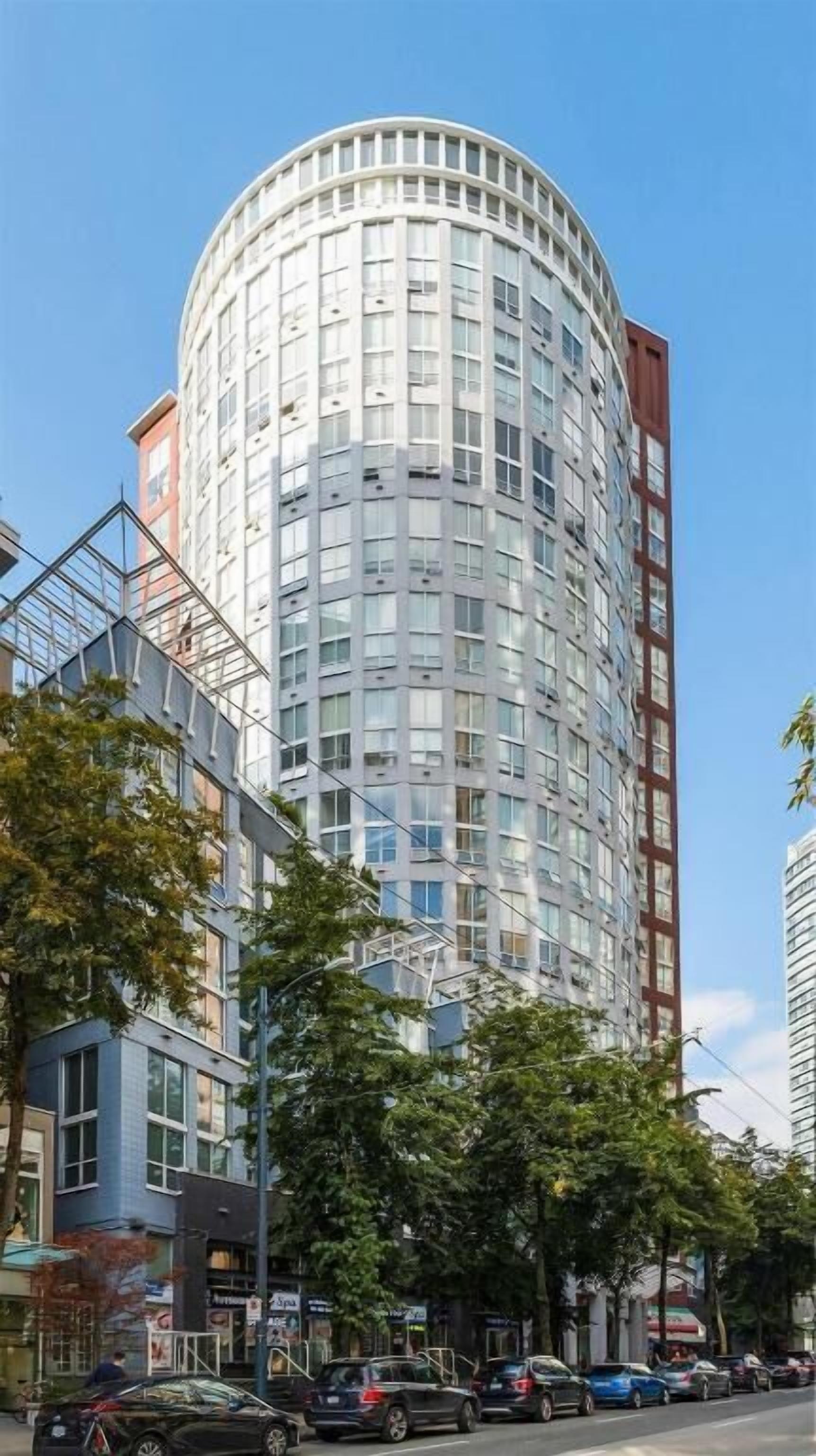 A modern high-rise building with a cylindrical shape, featuring a glass facade and multiple balconies.
