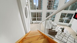 Un intérieur moderne avec un escalier en bois, une balustrade en verre et une vue sur les gratte-ciel, visible à travers de grandes fenêtres.