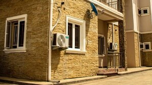 A multi-story residential building with stone facade, multiple air conditioning units, and a balcony. - Hilton Summer Apartments (Abuja)
